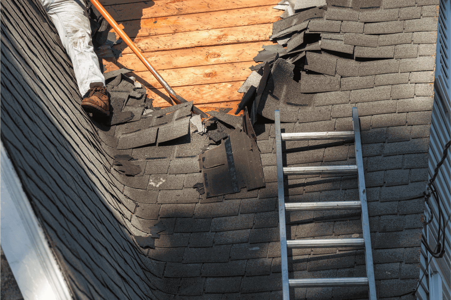 A worker using a roofing shovel to remove old shingles from a roof