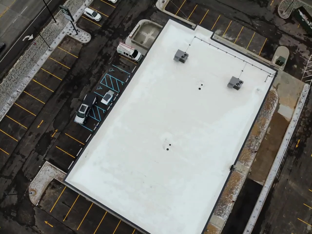 Can A Commercial Roof Inspection Help Protect Your Building in South Bend, IN? 2 An aerial, top-down drone view captures a flat, white commercial roof and its surrounding parking lot, showcasing the ideal perspective for a commercial roof inspection.
