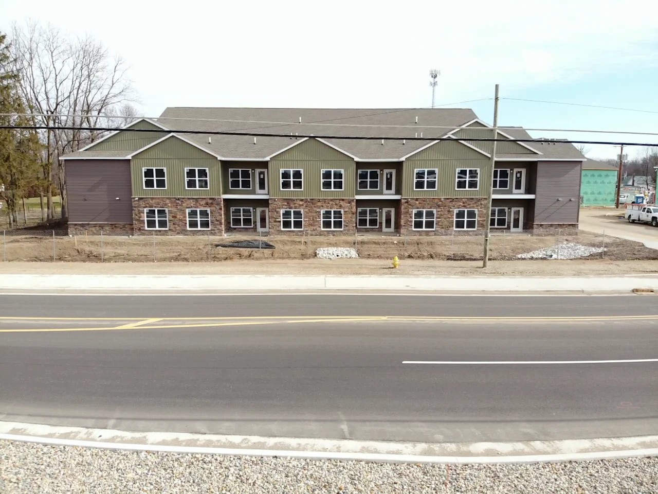 New Carlisle, IN 2 A wide shot captures a newly constructed multi-family commercial residential property featuring green siding, stone accents, and a neatly shingled roofline, showing a project completed with professional commercial roofing services.