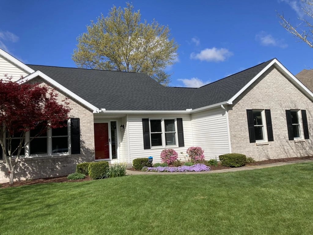 North Liberty, IN 3 A single-story home features light-colored brick siding, a vibrant red front door, and a freshly installed dark asphalt shingle roof, highlighting a property enhanced by professional exterior services.