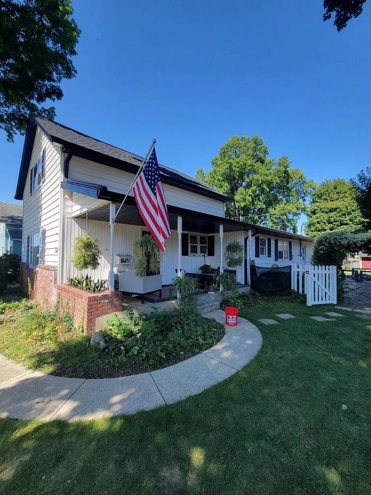 A charming white home with an American flag flying from the front porch features prominent black trim and downspouts, demonstrating a property protected by professional gutter services.