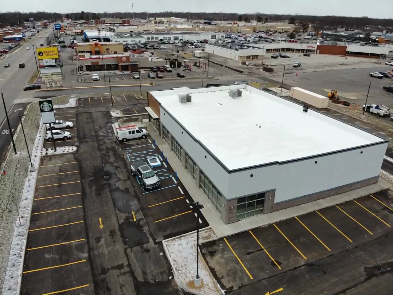 Niles, MI 2 An aerial view captures a modern retail building featuring a large, flat white roof system and an adjacent parking lot, illustrating a property built for reliable commercial roofing services.