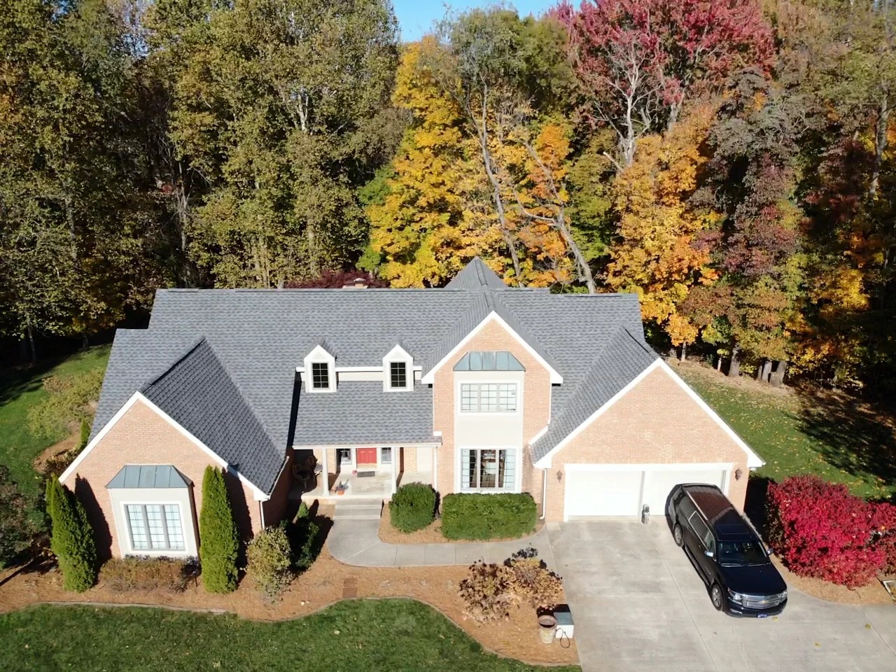 Niles, MI 3 An aerial shot showcases a beautiful brick home with a pristine shingle roof and a concrete driveway nestled against vibrant autumn foliage, illustrating the value of professional exterior services.