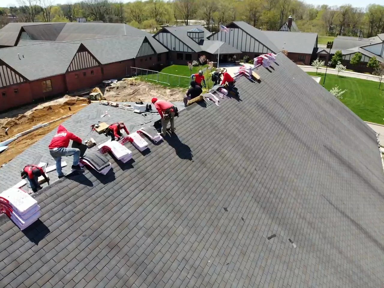 Lakeville, IN 2 An aerial view captures a professional roofing crew working on a large sloped facility roof lined with bundles of new shingles, highlighting a massive project completed with expert commercial roofing services.