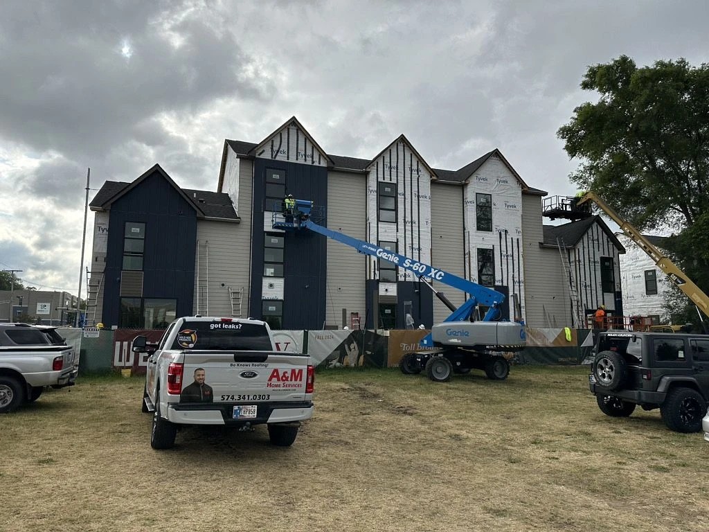 Notre Dame, IN 2 A branded service truck and a boom lift stand outside a multi-story building undergoing active construction, capturing a large project utilizing professional commercial roofing services.