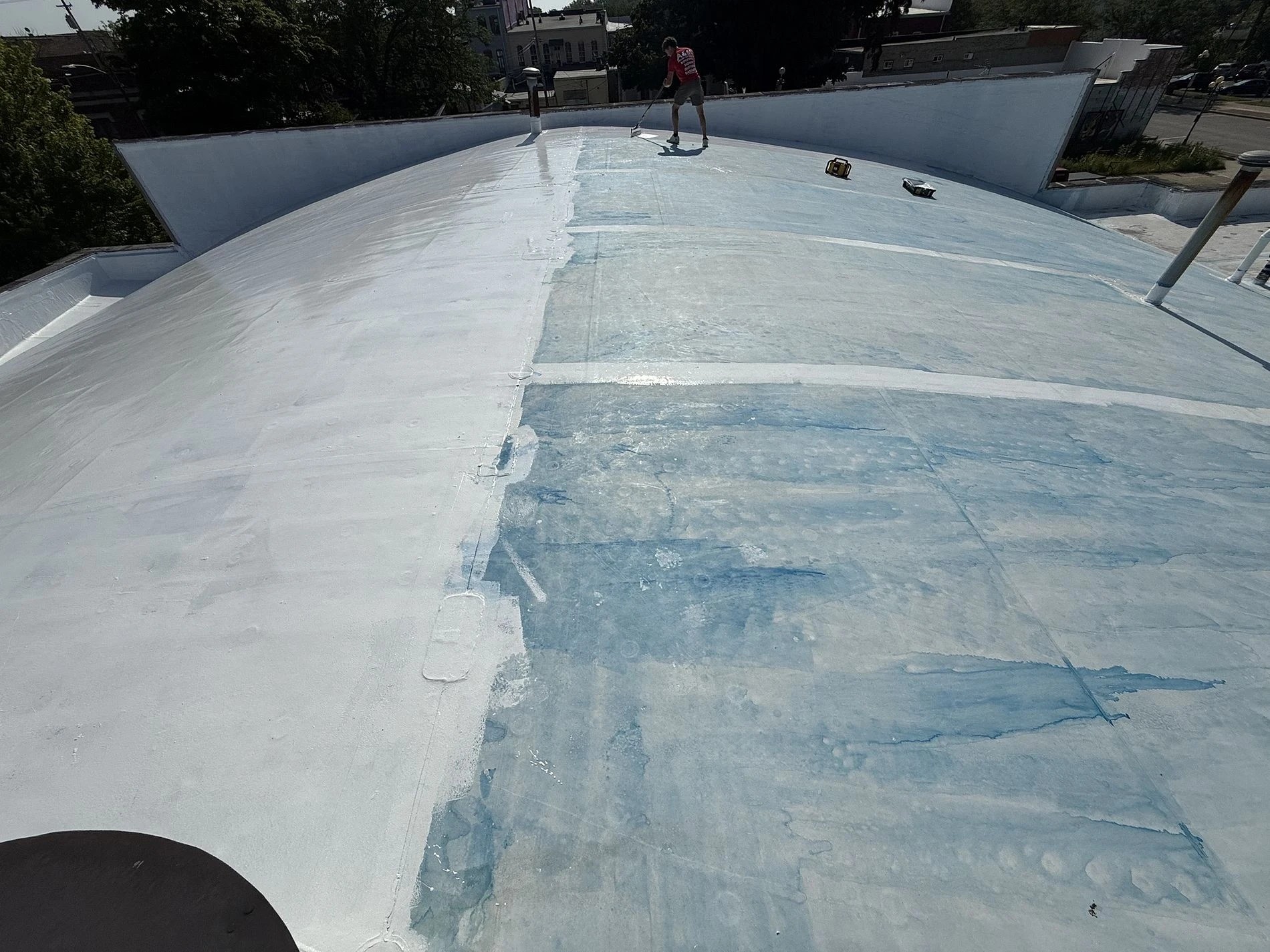 What Damages Flat Roofs Most In Elkhart, IN 2 A worker applies a white reflective coating as part of a commercial roof repair project on a wide curved roof.