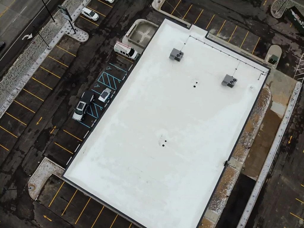 An overhead aerial view showcases a commercial building with a newly installed white flat membrane roof completed through expert roofing services.