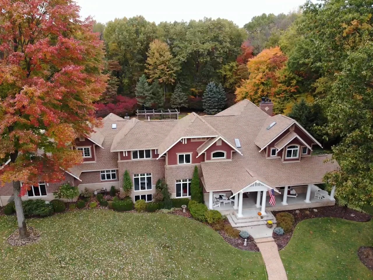 An aerial view shows a luxury home surrounded by autumn foliage, with pristine shingles, siding, and trim maintained by professional exterior services.