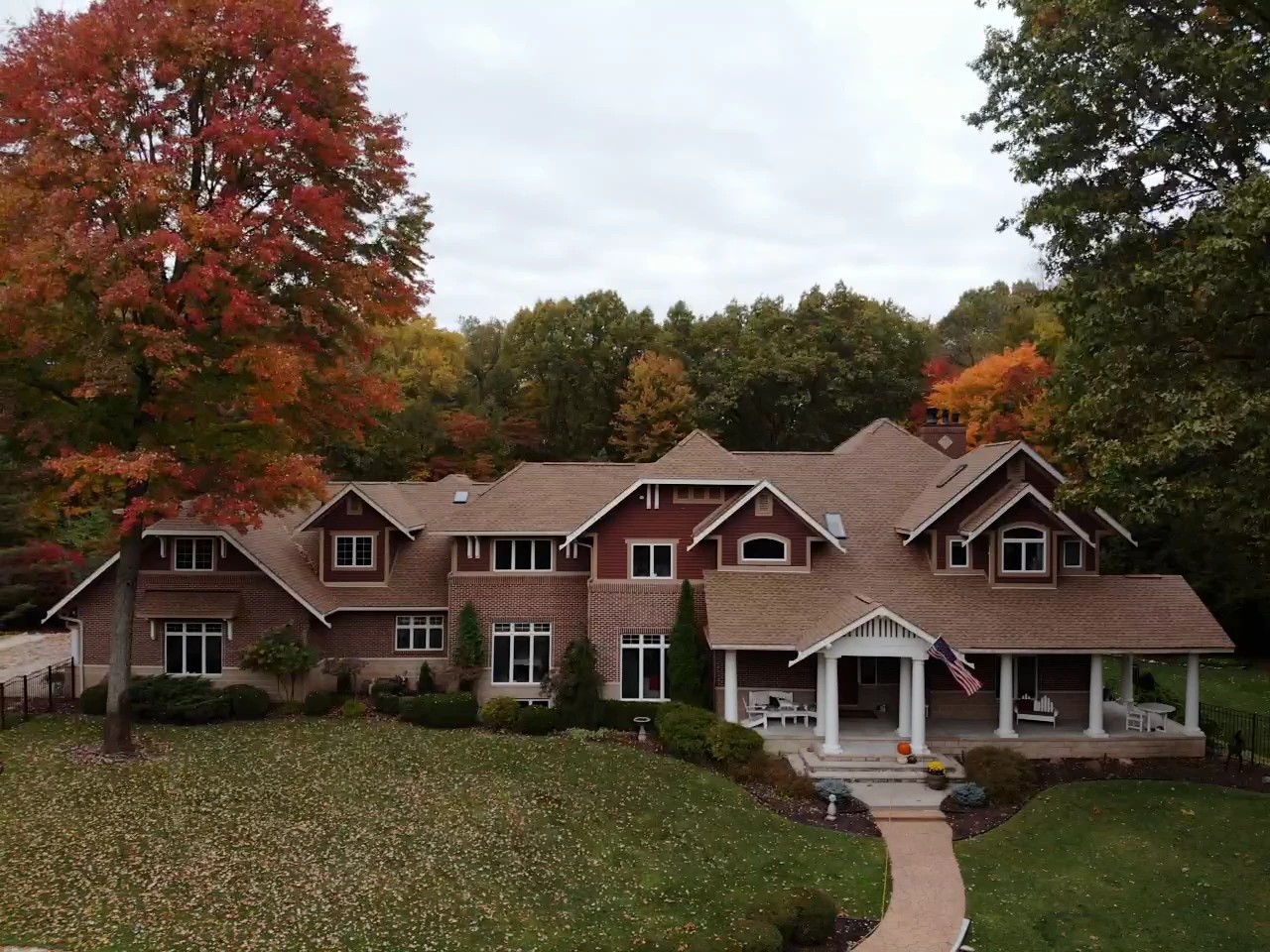 An aerial view showcases a grand multi-gabled home with expert roofing services surrounded by vibrant autumn trees.