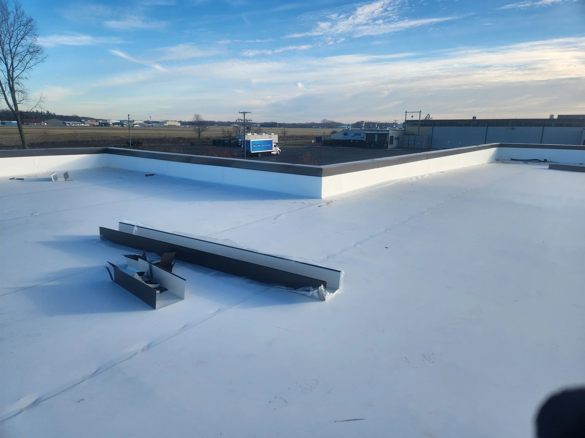 Lapaz, IN 2 A bright white flat membrane roof is under construction on a commercial building, showing materials and flashing installed during professional roofing services.