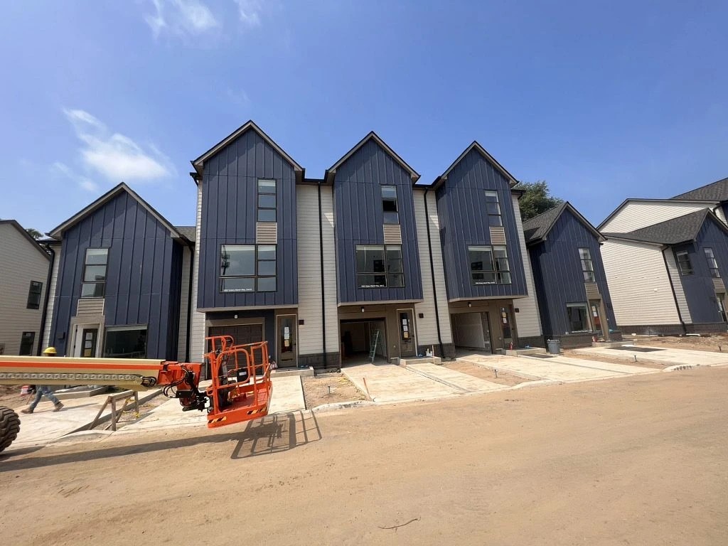 A line of modern, multi-story townhomes is under construction, featuring vertical metal siding and roof work, supported by professional exterior services.